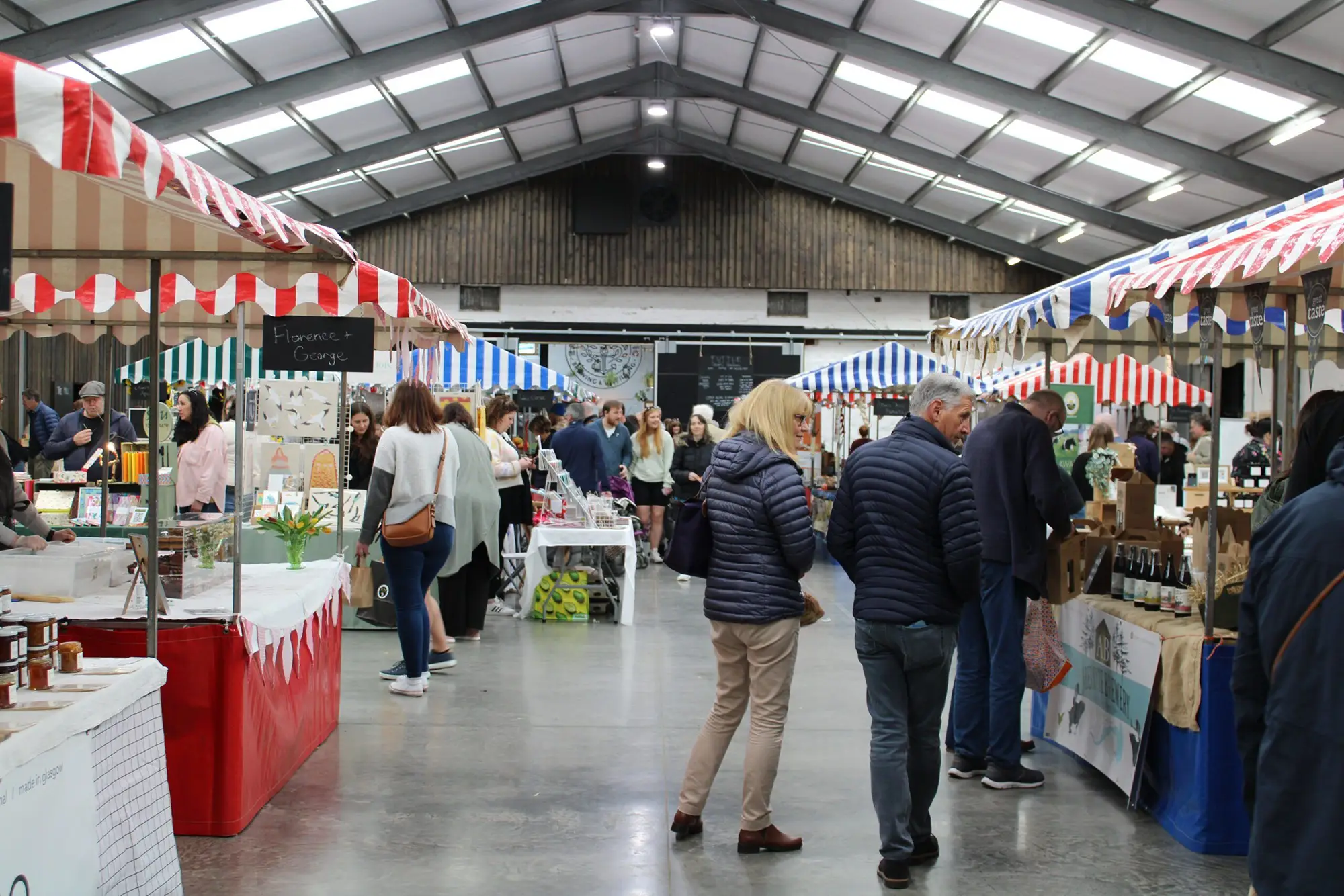 Shoppers at Bowhouse Market Weekend Shoppers walking between striped-awning stalls inside the Bowhouse market hall