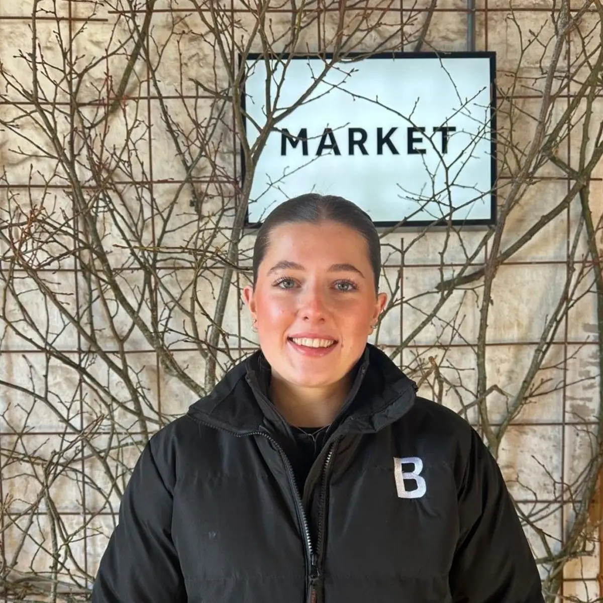 Caitlin Harrison, Bowhouse team Caitlin Harrison of the Bowhouse team, smiling beside the market sign