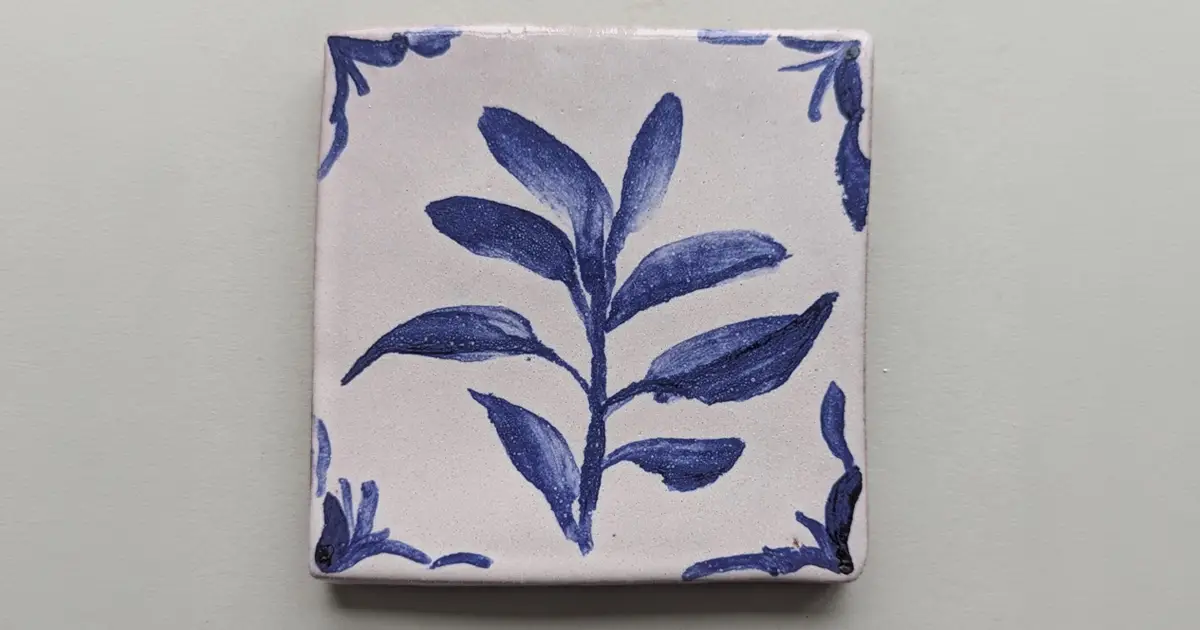 Hand-painted tile with a blue leafy branch design