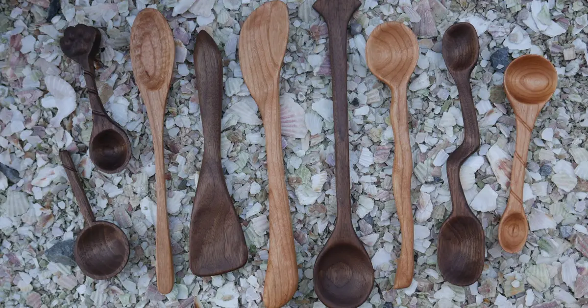 Row of hand-carved wooden spoons laid on gravel