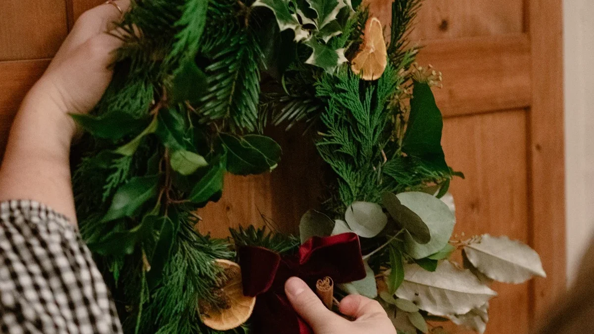 Hands adding foliage to a Christmas wreath hung on a wooden door