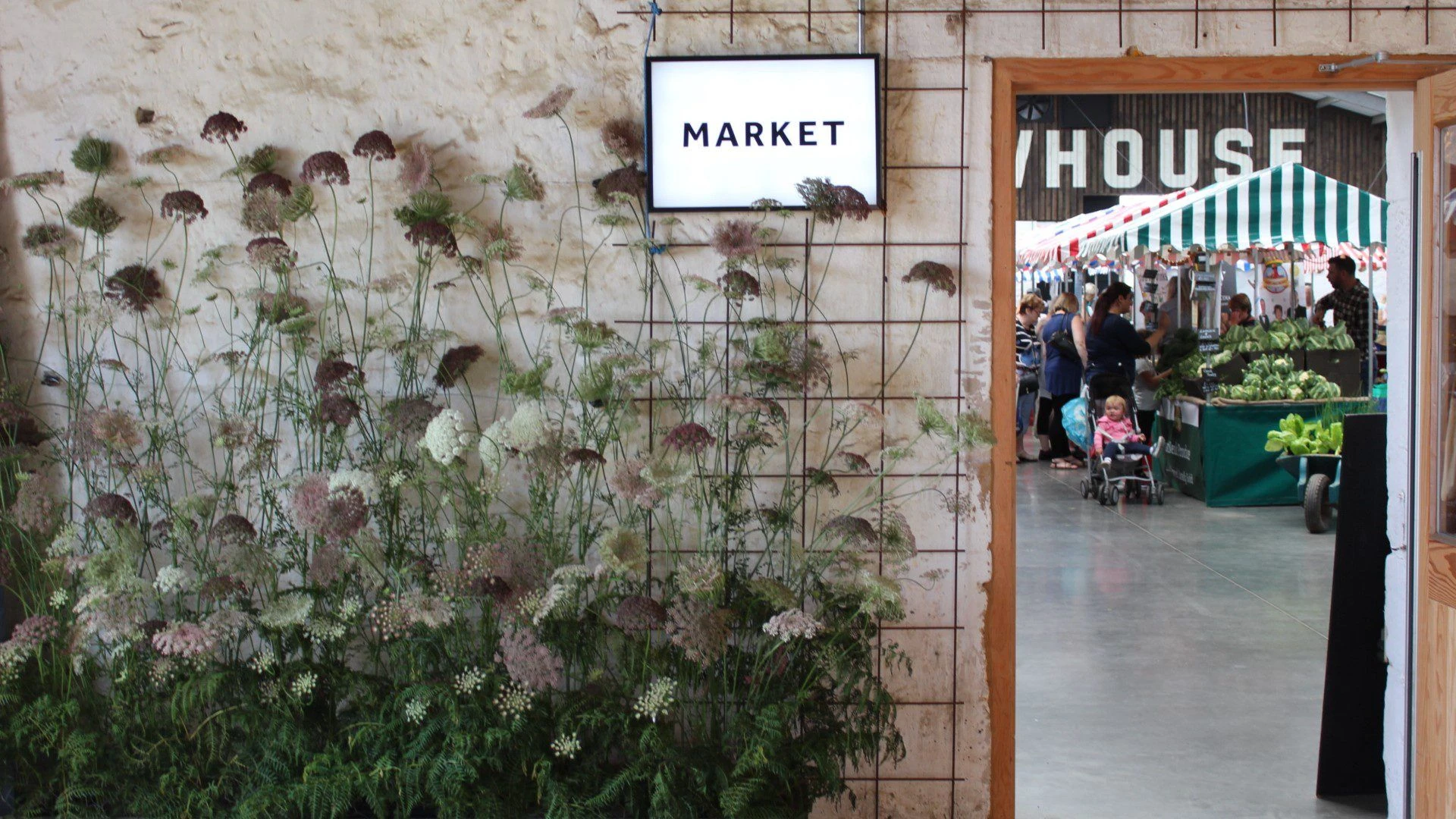 Market entrance at Bowhouse Market sign above a dried flower wall beside the doorway into the busy market hall